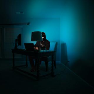 Une silhouette masquée travaillant sur un ordinateur dans l’obscurité, symbolisant les risques et les activités malveillantes dans l’univers numérique. © clint-patterson-unsplash