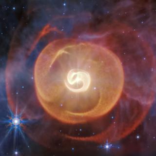 A imagem no infravermelho médio obtida pelo telescópio Webb revela pela primeira vez quatro envelopes de poeira enrolados em torno de um par de estrelas Wolf-Rayet chamadas Apep. Observações anteriores de outros telescópios mostraram apenas um. Os dados de Webb também confirmaram a existência de três estrelas ligadas gravitacionalmente. © Imagem: NASA, ESA, CSA, STScI; Ciência: Yinuo Han (Caltech), Ryan White (Universidade Macquarie); Processamento de imagem: Alyssa Pagan (STScI)