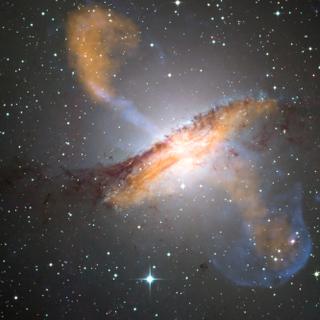 Uma imagem colorida de Centaurus A, revelando jatos emitidos pelo buraco negro central muito ativo da galáxia. Esta é uma imagem composta obtida com três instrumentos diferentes operando em comprimentos de onda diferentes. Os dados em 870 micrômetros, do Laboc, no Apex, são mostrados em laranja. Os dados de raios X, do Observatório Chandra, são mostrados em azul. Dados de luz visível obtidos pelo Wide Field Imager (WFI) do telescópio MGP/ESO de 2,2 metros, localizado em La Silla, Chile, mostram as estrelas. A linha de poeira característica da galáxia está próxima das “cores reais”. © ESO/WFI (Óptico); MPIfR/ESO/APEX/A.Weiss et al. (Submilimétrico); NASA/CXC/CfA/R. Kraft et al. (Raio X)