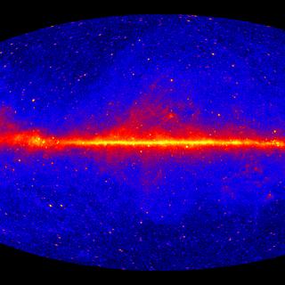 Esta imagem mostra todo o céu observado pelo Fermi Large Area Telescope (LAT). A característica mais marcante é o brilho difuso e brilhante que atravessa o centro do mapa e marca o plano central da nossa Galáxia, a Via Láctea. Os raios gama são produzidos principalmente pela colisão de partículas energéticas, aceleradas por ondas de choque de remanescentes de supernovas, com átomos de gás, ou mesmo com luz interestelar. Muitas estruturas semelhantes a estrelas acima e abaixo do plano da Via Láctea são galáxias distantes alimentadas por buracos negros supermassivos. A maioria das fontes brilhantes ao longo deste plano são pulsares. A imagem foi produzida a partir de 12 anos de observações utilizando raios gama de conversão frontal com energias superiores a 1 GeV. © NASA, DOE, Colaboração Fermi LAT