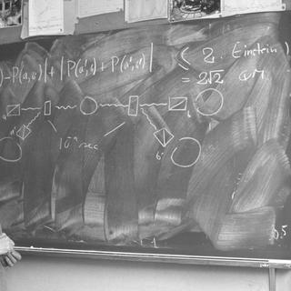 John Bell devant le tableau noir dans son bureau au Cern. On peut y voir tout en haut la fameuse inégalité qu'il a démontrée en 1964, au-dessus d'un schéma montrant le principe de l'expérience réalisée en 1982 avec des paires de photons polarisés par Alain Aspect et ses collègues. © Cern