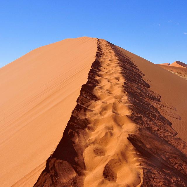 Le Sossusvlei est un désert de sel et d’argile situé dans le Parc national de Namib-Naukluft, dans le désert de Namib, en Namibie. Là se dressent de majestueuses dunes qui culminent à plus de 375 mètres de haut, leur permettant de figurer au palmarès des plus hautes dunes du monde.Leur couleur rouge qui contraste si joliment avec le bleu du ciel local, elles la doivent à la présence dans leur sable de trioxyde de fer (Fe2O3). Du sable de grès érodés accumulé sur le site par des vents qui l’ont porté parfois sur des distances incroyables. Une partie viendrait même du désert du Kalahari.© Sue Kellerman, Flickr, CC by-NC 2.0
