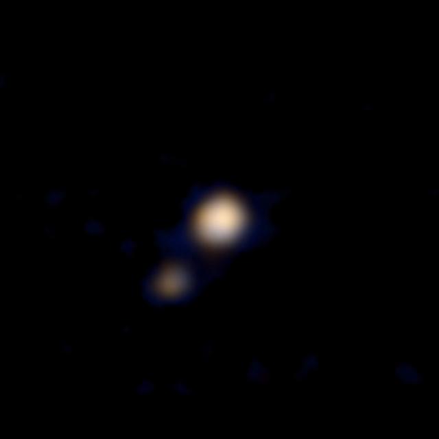 Le système Pluton-Charon photographié le 9 avril 2015 par l’instrument Ralph à bord de la sonde New Horizons à 115 millions de km (la distance Soleil-Vénus). Derrière la même optique, Ralph comporte en fait deux instruments, dont le MVIC, Multicolor Visible Imaging Camera, sensible dans le domaine visible et dans le proche infrarouge, à qui l&#39;on doit ce premier double portrait en couleurs. Il est flou mais augure bien de la qualité des observations effectuées lors du survol du 14 juillet prochain. Au plus près de Pluton, à environ 12.500 km, la résolution de Ralph/MVIC atteindra&amp;nbsp;5 km par pixel en couleurs et 500 m en monochrome. © Nasa, Johns Hopkins University Applied Physics Laboratory (JHUAPL), Southwest Research Institute